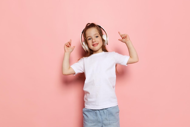 Portrait d'une belle petite fille enfant écoutant de la musique dans des écouteurs s'amusant isolé sur fond de studio rose