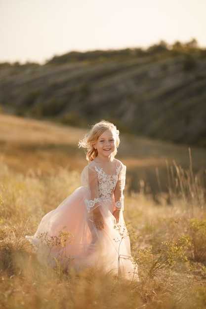 Portrait d'une belle petite fille princesse vêtue d'une robe rose. Posant dans un champ au coucher du soleil