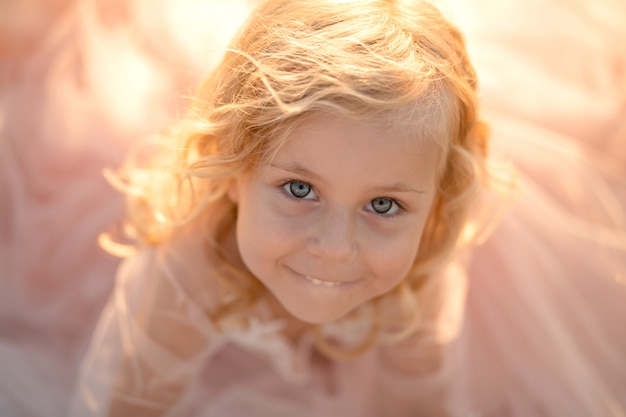 Portrait d'une belle petite fille princesse vêtue d'une robe rose. Posant dans un champ au coucher du soleil