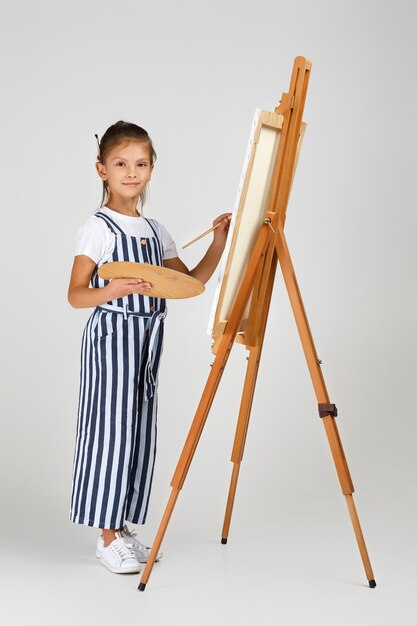 Portrait d'une belle petite fille tenant une palette d'art en bois et un pinceau sur fond de studio