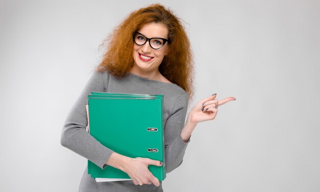 Portrait, de, belle rousse, jeune femme, dans, gris, vêtements, dans, lunettes, tenue, dossiers, sur, mur gris