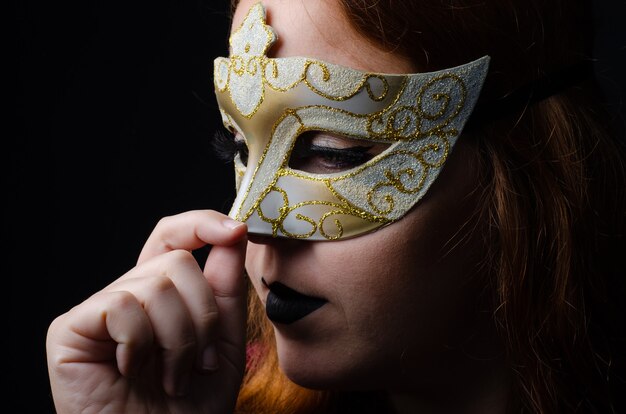 Portrait d'une belle rousse avec un masque vénitien fait dans un studio, image discrète, avec fond noir.