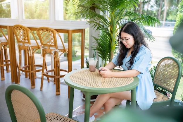 Un portrait d'une belle voyageuse asiatique heureuse vêtue d'une belle robe bleue style de vie appréciant la tenue à l'aide d'un téléphone portable décontracté travaillant dans un café assis sur fond de restaurant