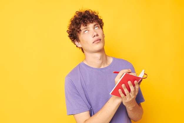 Portrait d'un bloc-notes jeune homme bouclé avec un stylo apprenant des émotions fond isolé inchangé