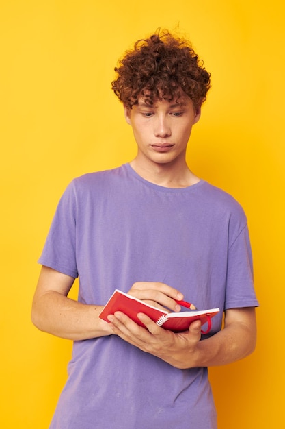 Portrait d'un bloc-notes jeune homme bouclé avec un stylo apprenant des émotions fond isolé inchangé