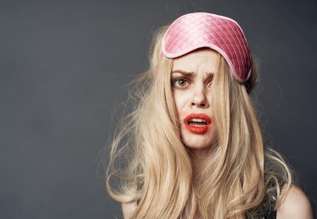 Portrait d'une blonde dans un masque de sommeil et un rouge à lèvres de maquillage brillant enduit sur son visage