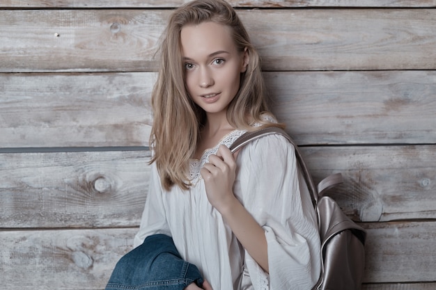 Portrait blonde jeune femme avec sac à dos argenté sur mur en bois