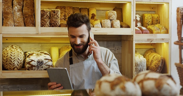 Portrait de boulanger heureux travaillant dans une boulangerie à l'aide d'un ordinateur tablette numérique et parler au téléphone cellulaire