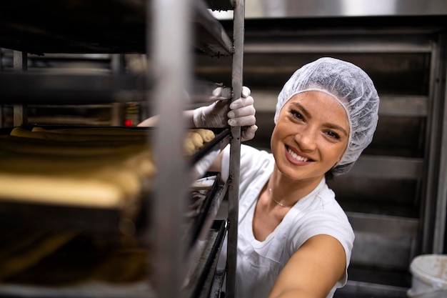 Portrait d'une boulangère en uniforme blanc propre et filet à cheveux préparant du pain dans la production de boulangerie