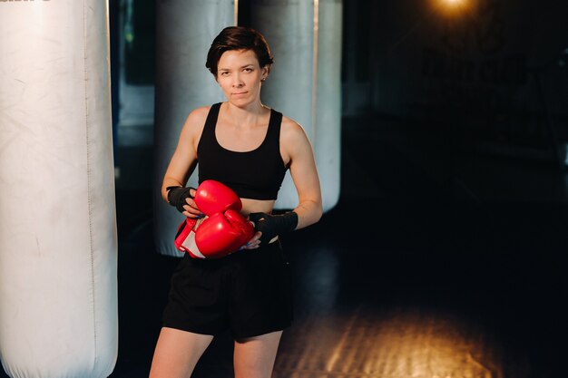 Portrait d'une boxeuse en gants rouges dans la salle de sport pendant l'entraînement