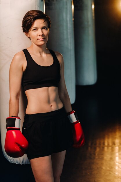 Portrait d'une boxeuse en gants rouges dans la salle de sport pendant l'entraînement