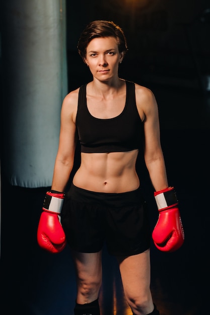 Portrait d'une boxeuse en gants rouges dans la salle de sport pendant l'entraînement