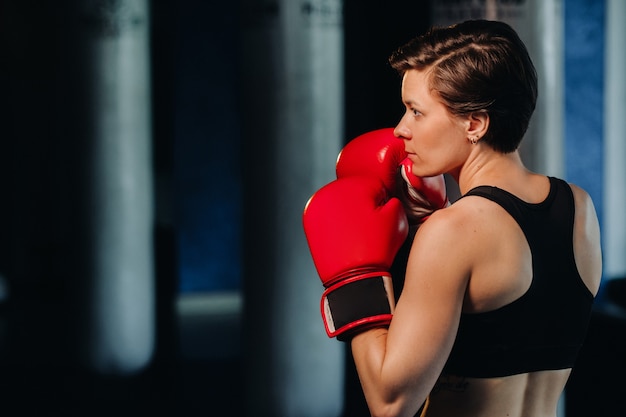 Portrait d'une boxeuse en gants rouges dans la salle de sport pendant l'entraînement