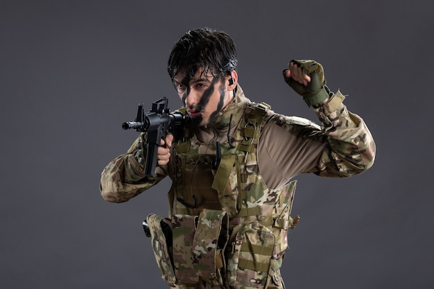 Portrait de brave soldat en camouflage avec mitrailleuse sur mur sombre