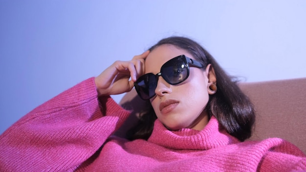 Photo portrait d'une brune élégante dans un pull rouge et des lunettes de soleil se trouve sur un fond bleu clair