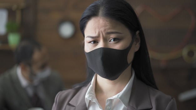 Portrait de brune inquiète au masque au bureau