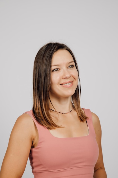 Portrait de brunette souriante Belle jeune femme heureuse posant sur fond gris isolé en studio, elle porte un haut beige pour le yoga ou le fitness vue latérale