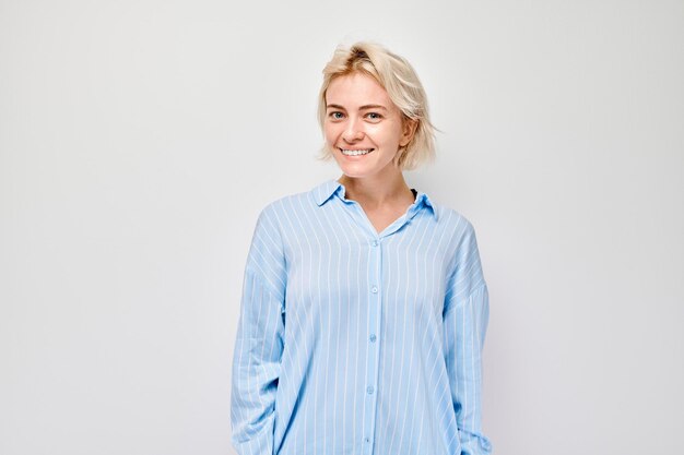 Portrait caucasien jeune femme blonde souriant joyeusement isolé sur fond blanc studio Bonne fille en chemise bleue avec expression du visage heureux