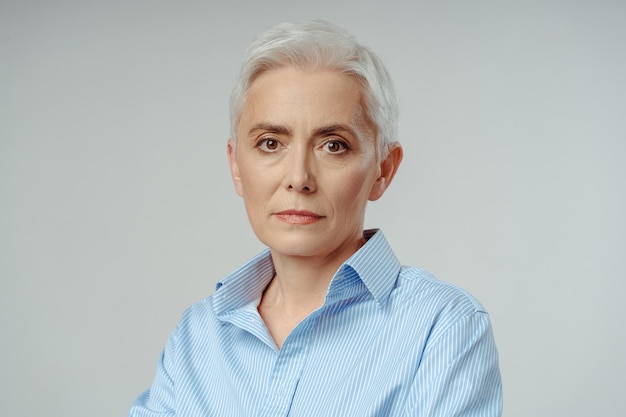 Portrait Caucasienne attrayante confiante femme d'affaires âgée aux cheveux gris regardant la caméra avec un visage sérieux debout sur un fond gris isolé