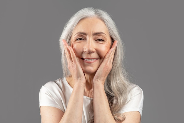 Portrait d'une charmante femme âgée regardant la caméra et souriant touchant la peau lisse sur son visage