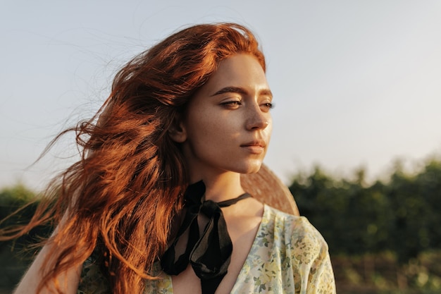 Portrait d'une charmante fille aux cheveux roux brillants, de belles taches de rousseur et un bandage sombre sur le cou en détournant les yeux et posant en plein air