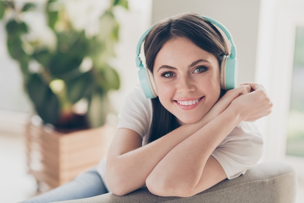 Portrait d'une charmante fille avec un casque sans fil assis sur le canapé regarde à huis clos à pleines dents souriant dans la maison à l'intérieur