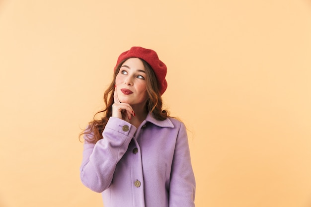 Portrait de charmante jeune fille des années 20 en manteau et chapeau souriant, tout en se tenant isolé