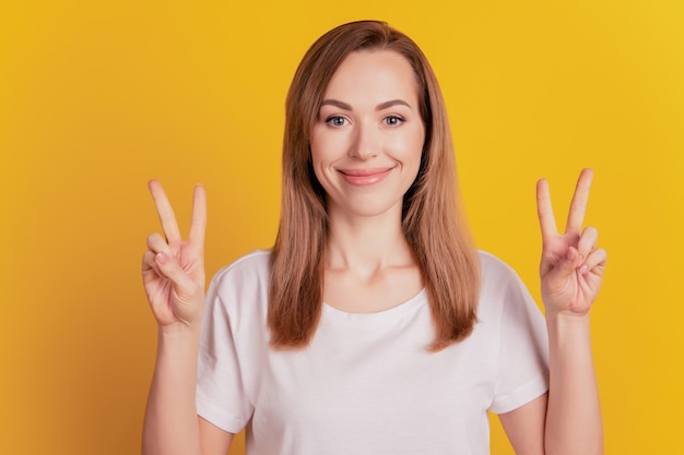 Portrait de charmante jeune fille montrer signe de paix isolé sur fond jaune