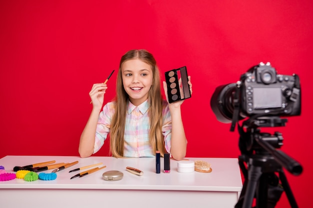 Portrait de charmante petite fille se filmant à la table avec des cosmétiques