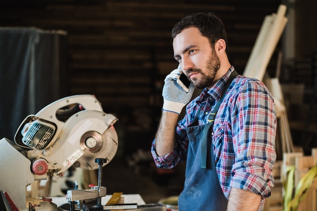 Portrait de charpentier appelant par téléphone intelligent à l'atelier