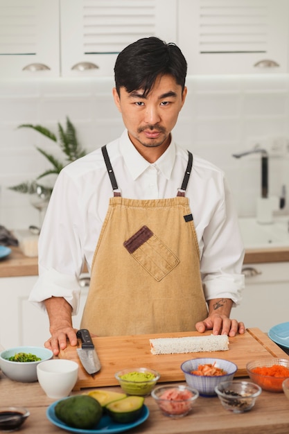 Portrait de chef asiatique regardant la préparation de sushi caméra avec tapis de bambou et ingrédients sushi