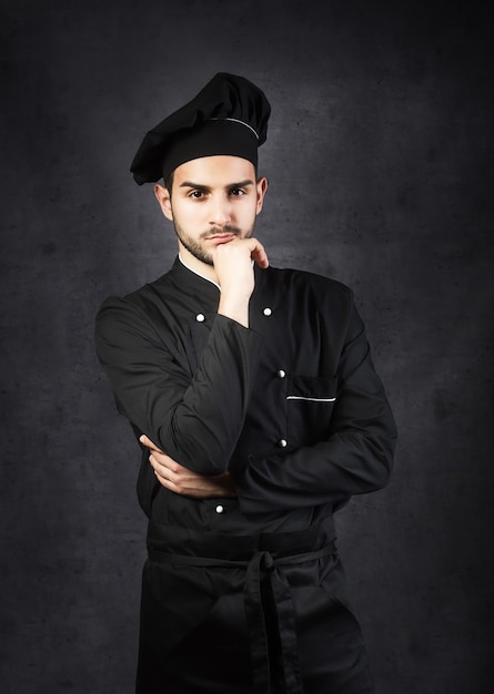 Portrait d'un chef cuisinier sur fond gris uniforme noir