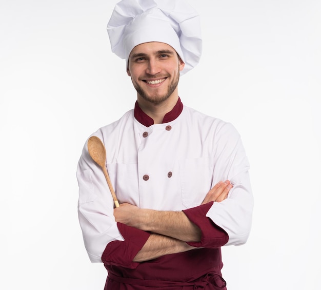 Portrait d'un chef cuisinier positif à pleines dents en béret, tenue blanche ayant des outils dans les bras croisés regardant la caméra isolée sur fond blanc.