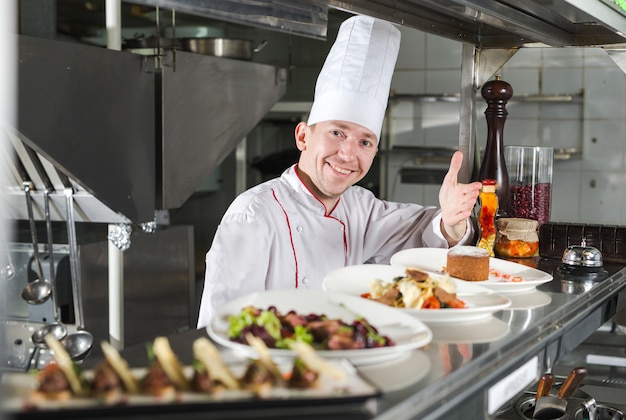 Portrait d'un chef avec des plats cuisinés dans la cuisine du restaurant.