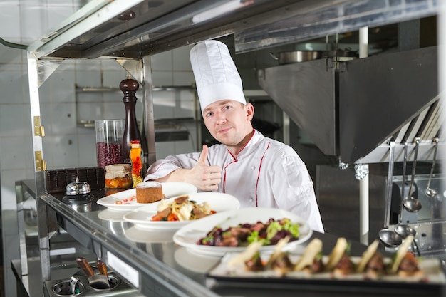 Portrait d'un chef avec des plats cuisinés dans la cuisine du restaurant.