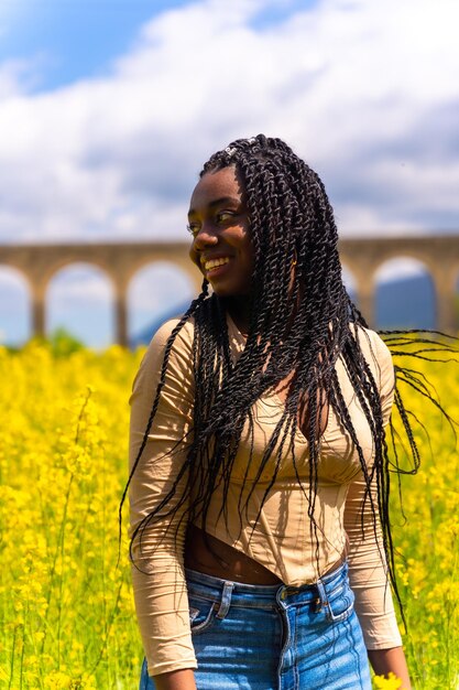 Portrait de cheveux en mouvement de style de vie d'une fille ethnique noire avec un voyageur de tresses dans un champ de fleurs jaunes