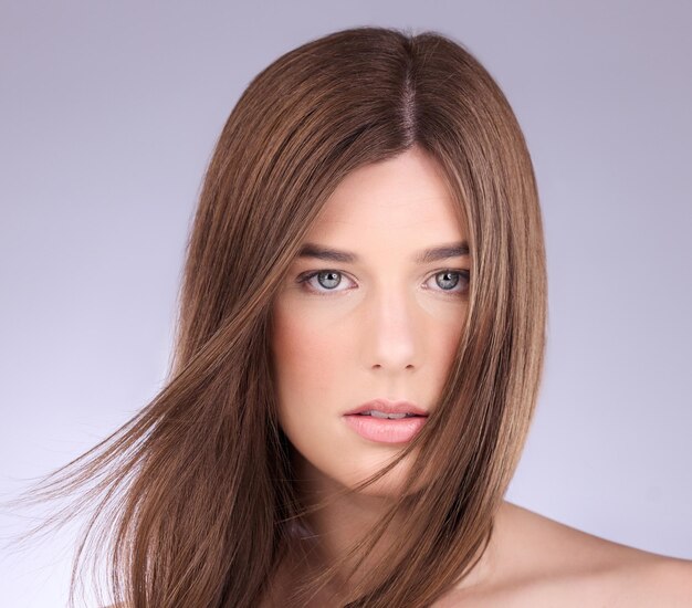 Portrait cheveux et vent avec une femme modèle en studio sur fond gris pour le soin des cheveux ou le traitement à la kératine Salon de shampoing et beauté avec une jolie jeune femme posant dans une brise sur un mur