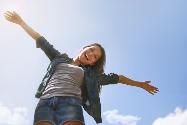 Portrait ciel bleu et bras avec une femme en plein air dans la nature pour s'amuser en liberté ou aventure en été d'en bas Sourire santé et bien-être avec une jeune femme heureuse à l'extérieur pour célébrer la vie