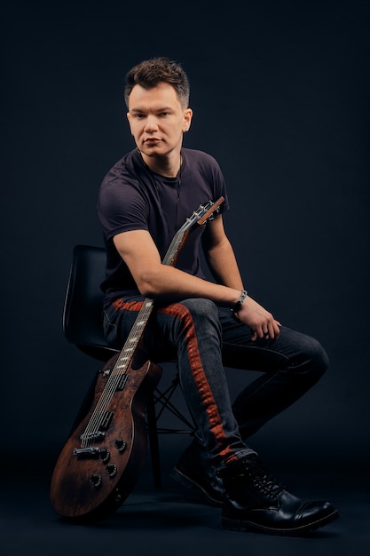 Photo portrait clé faible du musicien assis sur une chaise avec guitare