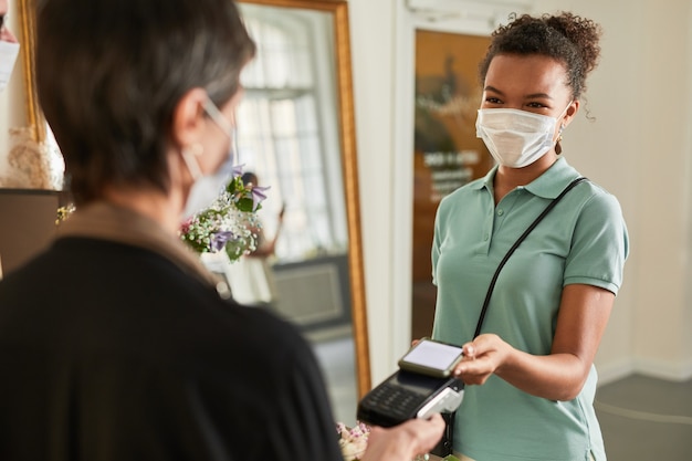 Portrait d'une cliente payant via un smartphone dans un magasin de fleurs et portant un espace de copie de masque