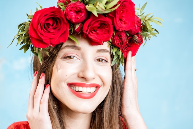 Portrait coloré d'une belle femme en robe rouge avec une couronne de roses rouges sur fond bleu