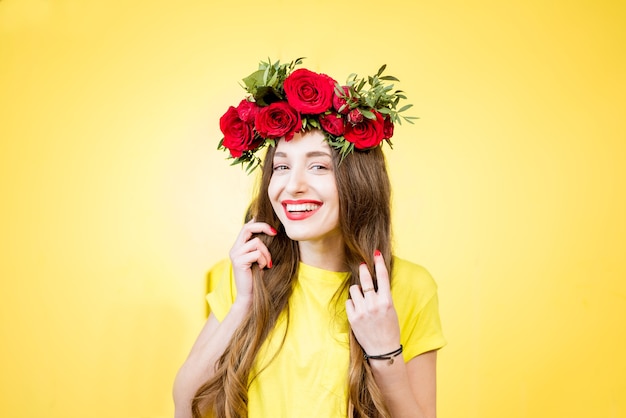 Portrait coloré d'une belle femme en t-shirt jaune avec une couronne de roses rouges sur fond jaune