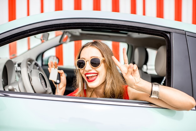 Portrait coloré d'une jeune femme heureuse tenant une clé en tirant la fenêtre de la voiture sur le fond du mur rouge