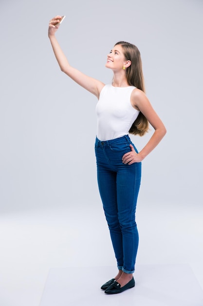 Portrait complet d'une adolescente heureuse faisant une photo de selfie sur un smartphone isolé