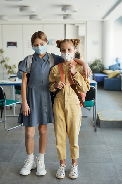 Portrait complet de deux filles portant des masques dans une salle de classe et regardant la caméra, mesures de sécurité covid