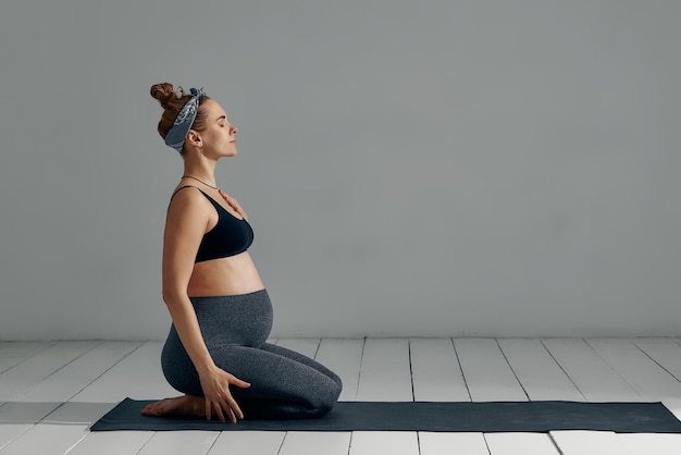 Portrait complet du corps d'une femme enceinte faisant du yoga sur un tapis d'exercice isolé sur fond gris