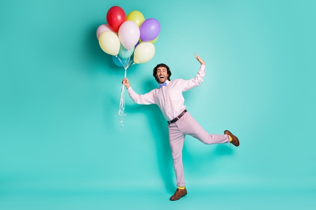 Portrait complet du corps d'un homme génial et étonné montrant des vêtements de cérémonie habillés de mouche tenir des ballons isolés sur fond de couleur turquoise