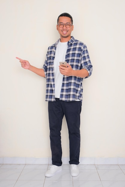 Portrait complet du corps d'un homme pointant vers le côté droit tout en tenant un téléphone portable