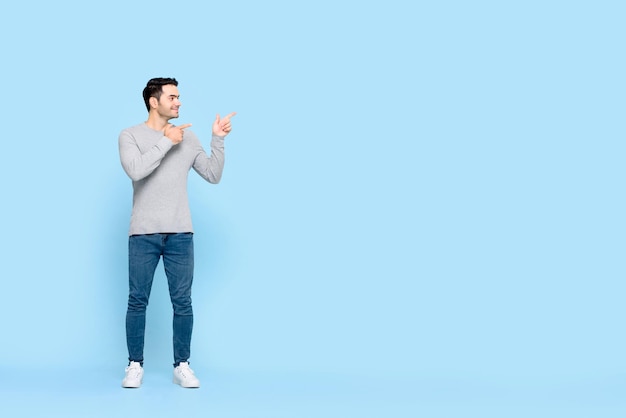 Portrait complet du corps d'un jeune homme caucasien souriant et joyeux dans des vêtements décontractés pointant les mains de côté pour copier l'espace sur fond bleu clair