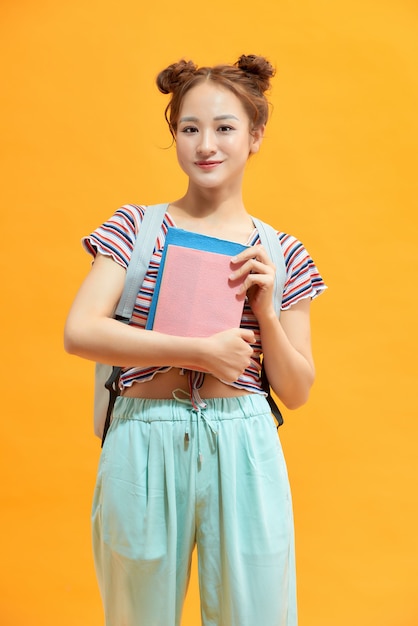 Portrait complet d'une étudiante avec un sac à dos et des livres isolés sur fond jaune